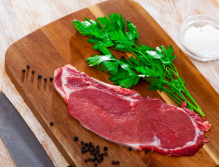 Raw piece of beef tenderloin with spices on wooden cutting board on light background