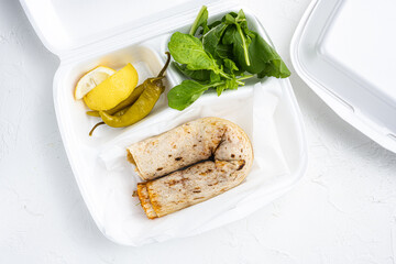 Doner kebab wrap in lavash bread, in plastic pack container delivery lunch box, on white stone...