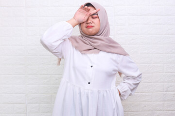 Asian Muslim woman wearing hijab dizzy and stressed with hands touching head isolated over white...