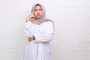 Young veiled muslim woman standing crossed arms putting a finger on the forehead looking up...