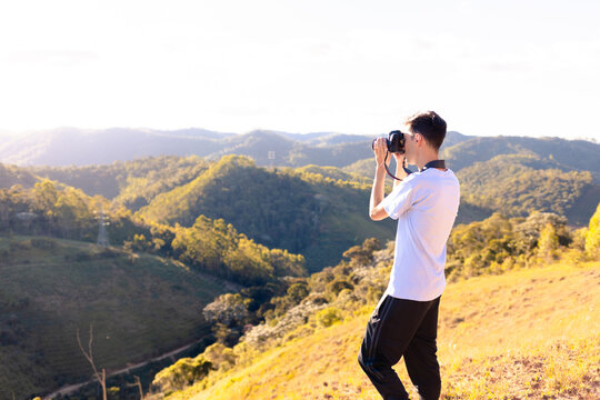 Photographer standing on top of a mountain taking pictures or filming the landscape of mountains with sunset.