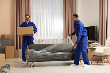 Male movers with cardboard box and sofa in new house