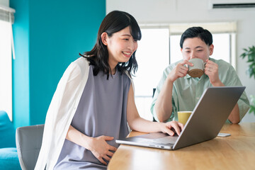 自宅でリモートワークをする妻と彼女を見守る夫
