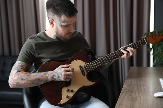 Handsome hipster man playing guitar in room