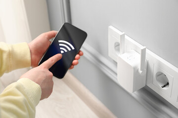 Woman with smartphone connecting to internet via wireless repeater indoors, closeup. Wi-Fi symbol...