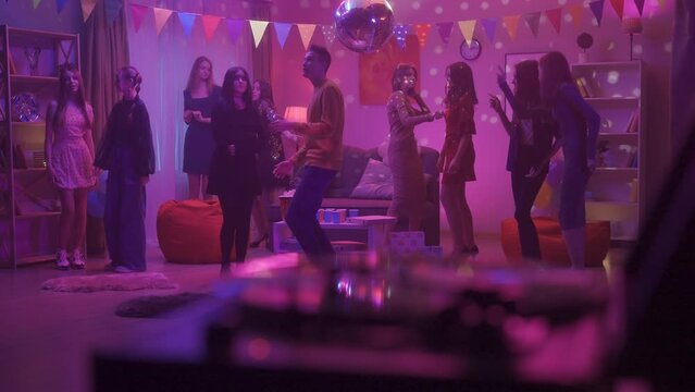 Friends at a party. Children dance in a room with a disco ball to music played from a retro turntable. The girl in black feels awkward, modestly dancing next to the guy. HDR BT2020 HLG Material.