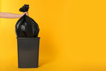 Woman holding trash bag full of garbage over bucket on orange background, closeup. Space for text - obrazy, fototapety, plakaty