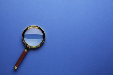 Magnifying glass on blue background, top view. Space for text