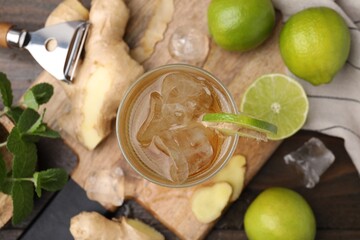 Glass of tasty ginger ale with ice cubes and ingredients on wooden table, flat lay
