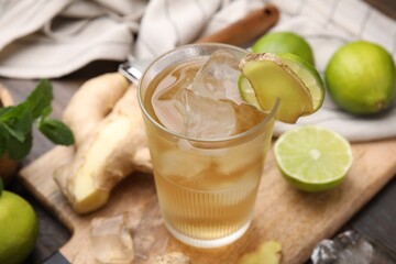 Glass of tasty ginger ale with ice cubes and ingredients on wooden table, closeup