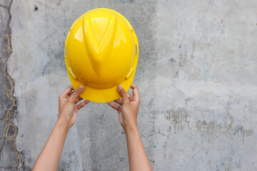 Hands holding a yellow safety helmet for construction project over grey concrete background 