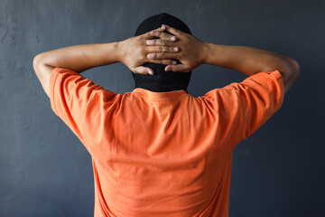 Back view of prisoner in orange t-shirt holding his hands behind his head, surender position over...