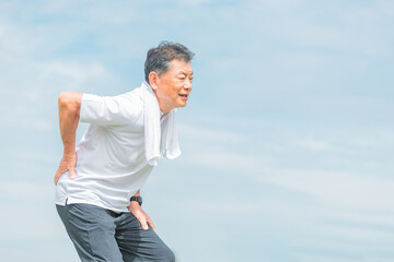 運動して腰を痛める高齢者・シニアのアジア人男性
