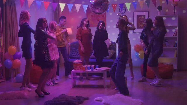 A group of friends are dancing vigorously at a party. The girl in black stands out among everyone with her informality, modesty and bashfulness. Party, birthday, celebration. HDR BT2020 HLG Material.