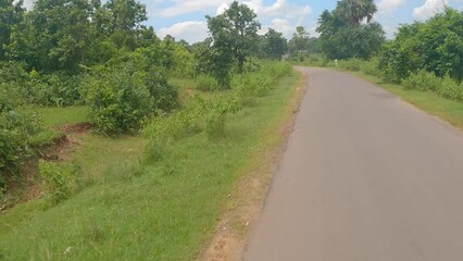 16th August, 2022, Belpahari, West Bengal, India: Beautiful village road of Bengal with few decorated village traditional houses. Paddy fields and forest both side of the road.