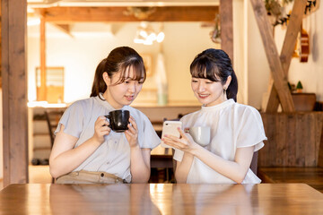 カフェでスマホを見ながら話す笑顔のアジア人女性
