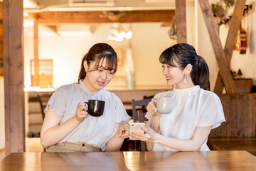 カフェでスマホを見ながら話す笑顔のアジア人女性

