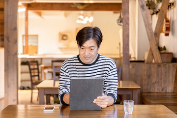 カフェでタブレットを使って仕事・リモートワークするアジア人の中年ビジネスマン
