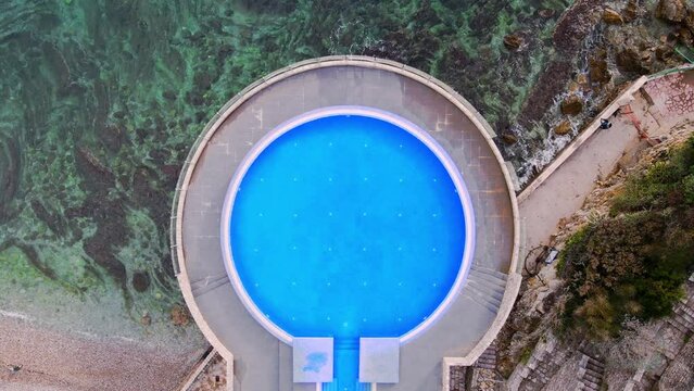 Aerial drone footage captures the captivating view of an empty round pool set against the breathtaking backdrop of the sea. Serene and tranquil, a picturesque scene to inspire and relax.