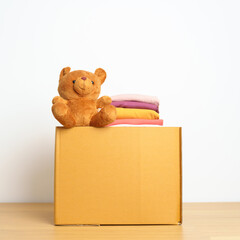 Kid Donation, Charity, Volunteer, Giving and Delivery Concept. Hand donate Bear doll and Clothes into cardboard box at home for support and help poor, refugee and homeless people. Copy space for text