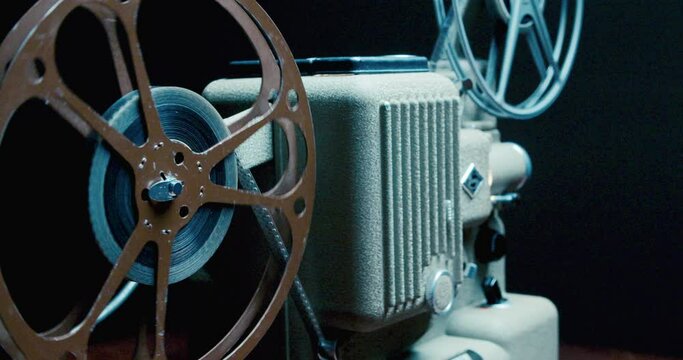 Old Movie Projector in Close up. Antique Movie Projector With 8mm Spinning Film Reels. Spinning Film Roll on a Vintage Film Projector. Light Beams From Film on an Old Projector 