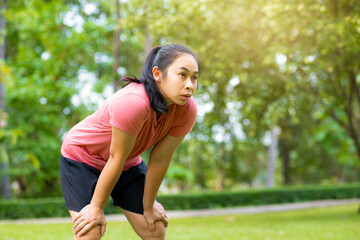 Young Asian woman standing bent over and breathing after running in the park. Young healthy woman...