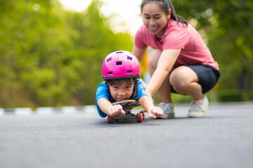 Active little girl and mom enjoy skateboarding. Cute little girl wearing helmet practicing skateboarding in park. Mother trains her daughter to skateboard. Outdoor sports for children.