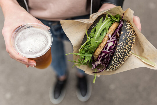 Close up of woman hands holding delicious organic salmon vegetarian burger and homebrewed IPA beer on open air beer an burger urban street food festival in Ljubljana, Slovenia