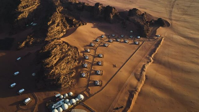 Deluxe desert resort in middle of mountains and wasteland, sunny evening in Wadi rum, Jordan - tilt, drone shot