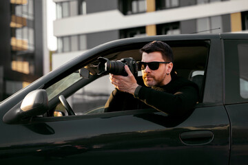 Man detective or agent taking photos from the car, wearing modern sunglasses 