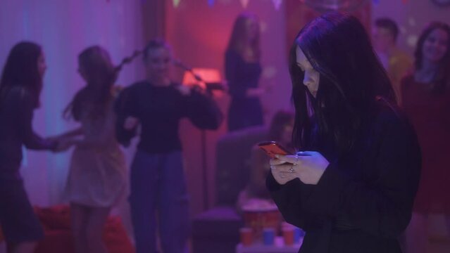 Goth girl watching video on phone, typing a message, checking social media while her friends are having fun at the party dancing. Single girl. Video 2 in 1. HDR BT2020 HLG Material.