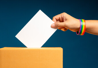 Election day. Hand voter holding ballot paper putting into the voting box at place election against a blue background