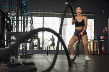 Fototapeta na wymiar Strong Asian woman doing exercise with battle rope at cross-fit gym. Athlete female wearing sportswear workout on grey gym background with weight and dumbbell equipment. Healthy lifestyle.