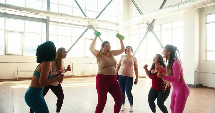Obese woman lifts dumbbells with effort standing in gym