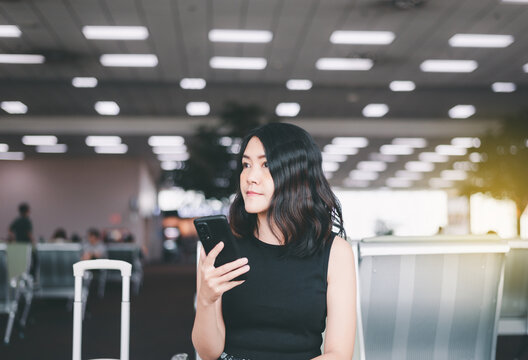 Woman passenger holding mobile phone and checking flight or online check in and travel planner at international airport