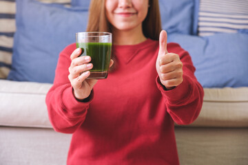 Portrait image of a young woman making thumb up hand sign while holding kale smoothie