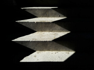Close-up of light and shadow on a staircase in the dark. black background. Stone stairs with abstract light. steps in the dark