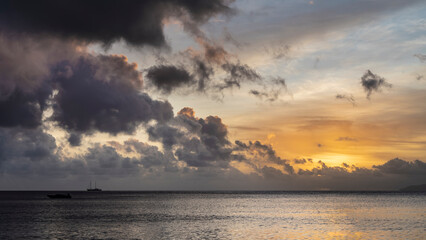 Beautiful tropical sunset. Purple clouds float in the sky, illuminated with gold. The silhouette of a ship on the horizon. Glare on the surface of the ocean. Seychelles.