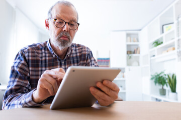 Senior caucasian man with glasses using digital tablet at home. Copy space.
