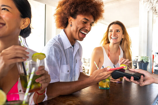 African American man paying at beach bar with phone. Black male paying round of drinks with mobile phone on vacation. - Powered by Adobe