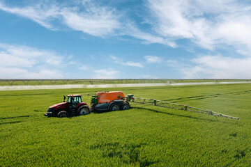 Aerial view of tractor spray fertilizer on green field. Farming tractor plowing and spraying on field.