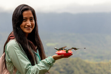 mujer latina bonita joven con colibries en bebedero en la mano sonriendo  © Lenin