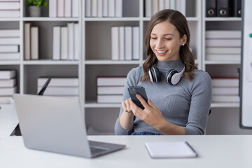 Young adult happy smiling Hispanic Asian student wearing headphones talking on online chat meeting using laptop in university campus or at virtual office. College female student learning remotely.
