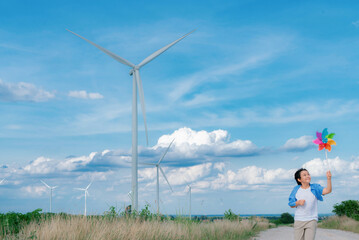 Progressive young asian boy playing with wind pinwheel toy in the wind turbine farm, green field...