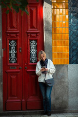 A woman is typing on her smartphone, at the door of a traditional Portuguese house.