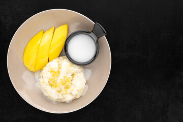 Khao Niaow Ma Muang, famous Thai dessert, top view shot of fresh ripe mango with sticky rice and coconut milk on the dark tone texture background