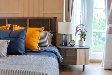 Yellow and blue pillow on cozy modern bedroom with carpet and side table lamp.