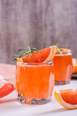 Fresh grapefruit juice with rosemary and pieces of fruit in glasses on the table vertical view