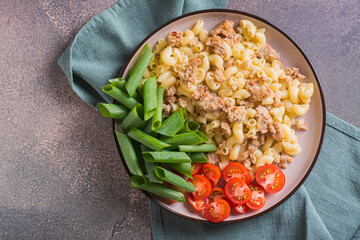 Close up of pasta with minced meat, tomatoes and green onions on a plate on the table top view