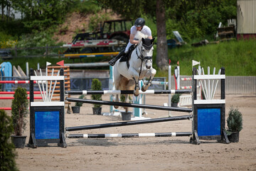 Show jumper with a white horse photographed from the front over an obstacle during a competition.